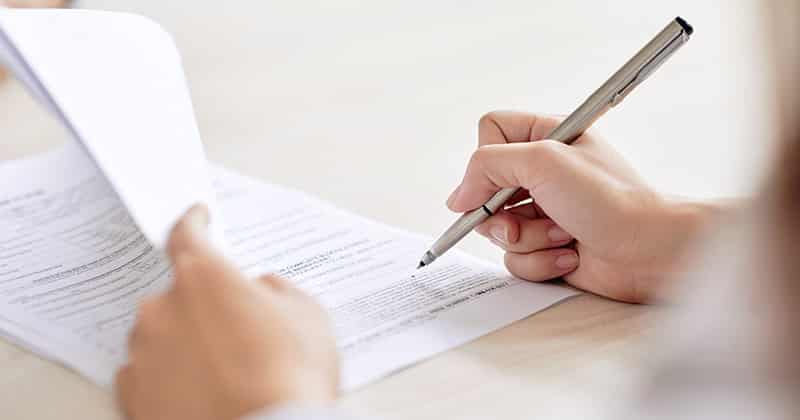 Crop shot of person with pen signing contract at desk